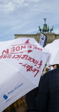 Sana Regio Kliniken mit weißen Regenschirmen "Unterfinanzierung beenden!"